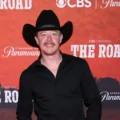 Adam Sanders has officially been crowned the first-ever champion of the inaugural season of the CBS reality competition series The Road. The high-stakes finale took place on Sunday evening, December 21, 2025, at the legendary Ryman Auditorium in Nashville, Tennessee. Sanders emerged victorious after competing against fellow finalists Cassidy Daniels and Channing Wilson in a night filled with emotional performances. The audience in attendance held the ultimate power to decide the winner after watching the finalists open for country music superstar Keith Urban one last time. This victory marks a significant turning point in the career of the Florida-born singer who has spent years working as a songwriter in the music industry. His triumph concludes a grueling nine-week journey where contestants traveled across the country to prove their talent on some of the most iconic stages in the nation. The finale broadcast showcased the immense talent of the top three artists through both cover songs and original compositions. Adam Sanders delivered a powerful rendition of the Brooks and Dunn classic That Ain’t No Way to Go which drew high praise from mentor Keith Urban for its emotional depth. He followed this performance with his original track All Summer Long which energized the crowd and highlighted his skills as an engaging live performer. Meanwhile, Channing Wilson impressed the audience with his grit while Cassidy Daniels took a bold risk by performing a rock-inspired cover. Despite the stiff competition, the audience response favored the consistent energy and vocal range that Sanders brought to the Ryman stage throughout the evening. The decision was announced during the closing moments of the episode as Urban revealed the results of the live audience vote to a cheering crowd. Winning the first season of The Road comes with a life-changing grand prize that will accelerate the career of Adam Sanders. The musician will receive a cash prize of two hundred and fifty thousand dollars along with a major recording contract and a Red Bull prize package. Perhaps most notably, Sanders has secured a prestigious performance slot at the 2026 Stagecoach Country Music Festival in California. He expressed profound gratitude after the announcement stating that the victory felt like a dream come true after years of being told no in the competitive music business. His background as a songwriter for artists like Luke Bryan and Dierks Bentley provided him with a unique perspective throughout the competition. This win validates his transition from a behind-the-scenes creator to a front-and-center superstar in the making. The success of the first season of The Road has solidified the show as a major player in the television landscape. Executive producers Blake Shelton and Taylor Sheridan designed the series to focus on the raw reality of life on tour for aspiring musicians. By having contestants open for Keith Urban in various cities, the show offered a unique look at the challenges and rewards of the country music circuit. The finale at the Ryman Auditorium served as a fitting conclusion to a season that prioritized authentic talent and audience connection over traditional judging panels. As Adam Sanders begins his new chapter as a recording artist, fans are already looking forward to the future of the franchise. The impact of the series on the careers of all three finalists suggests that The Road will continue to be a vital platform for discovering the next generation of music stars.
